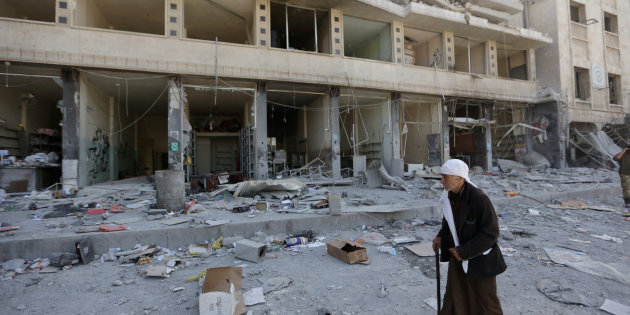 A Kurdish elderly man walks with a cane at a damaged site in Afrin