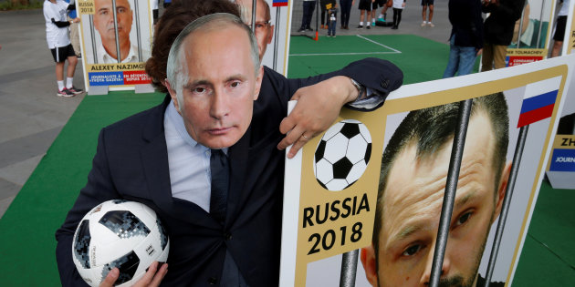A Reporter Without Borders (RSF) activist, wearing a mask depicting Russian President Vladimir Putin, stands next to a giant portrait of journalist Alexei Kungurov on Place de la Republique in Paris
